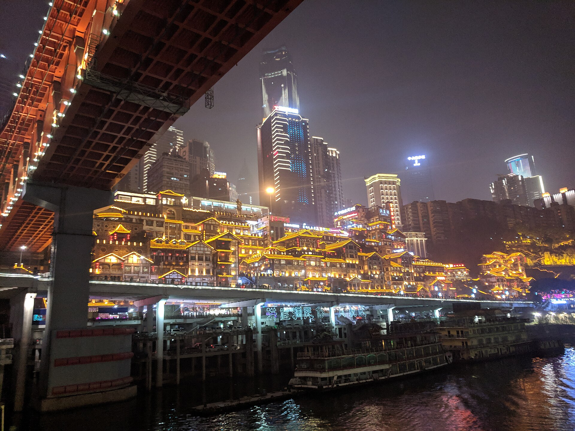 Hongya Cave glowing above the river and road after dark