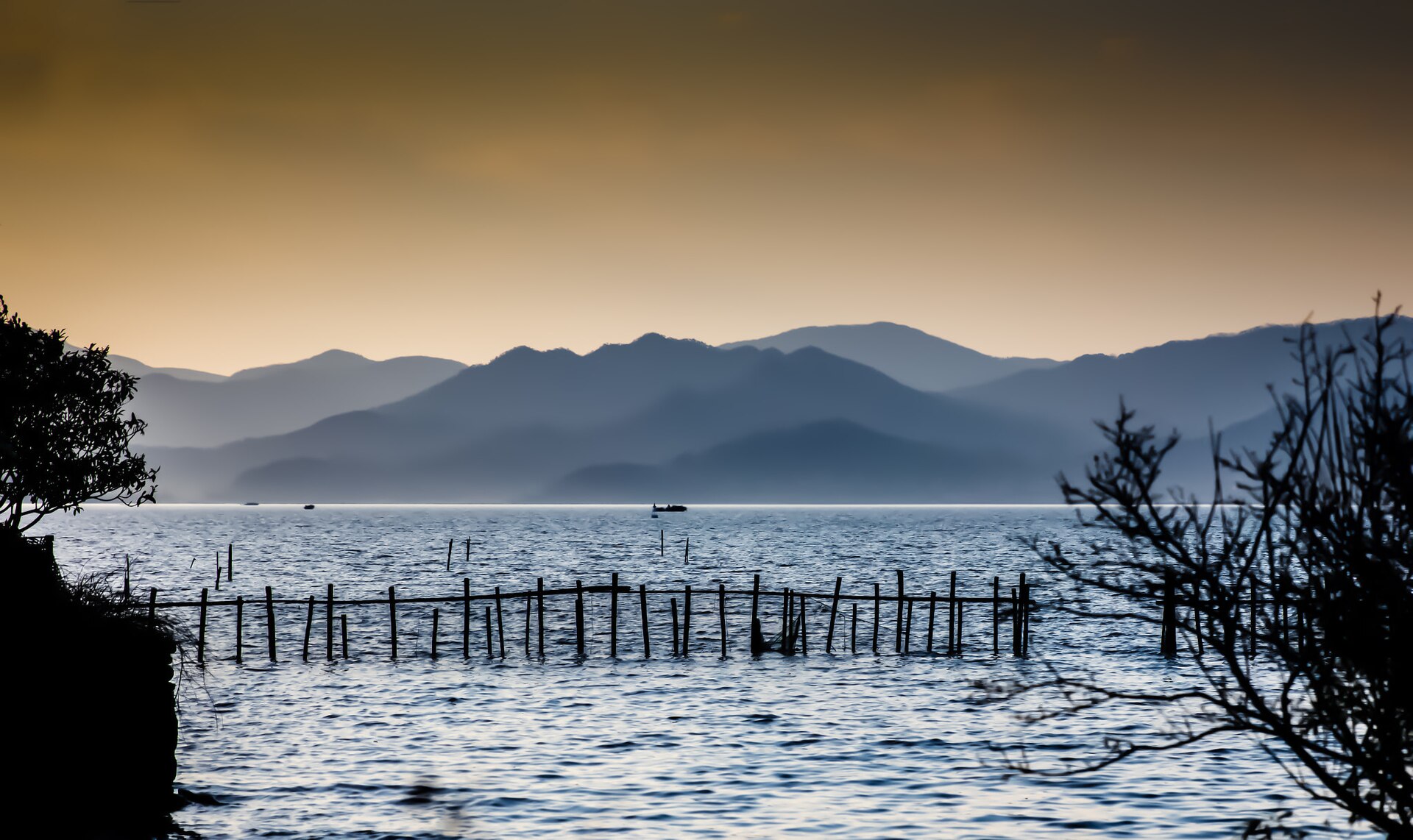Blue water, fishing stakes, and layered hills at Dongqian Lake in Ningbo